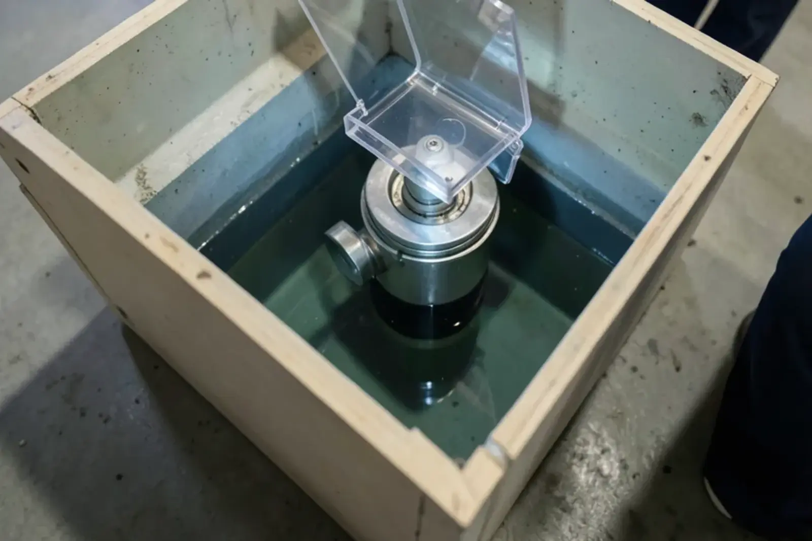 Open access box in a basement floor showing the clear cover and internal flap of a backwater valve on the building drain