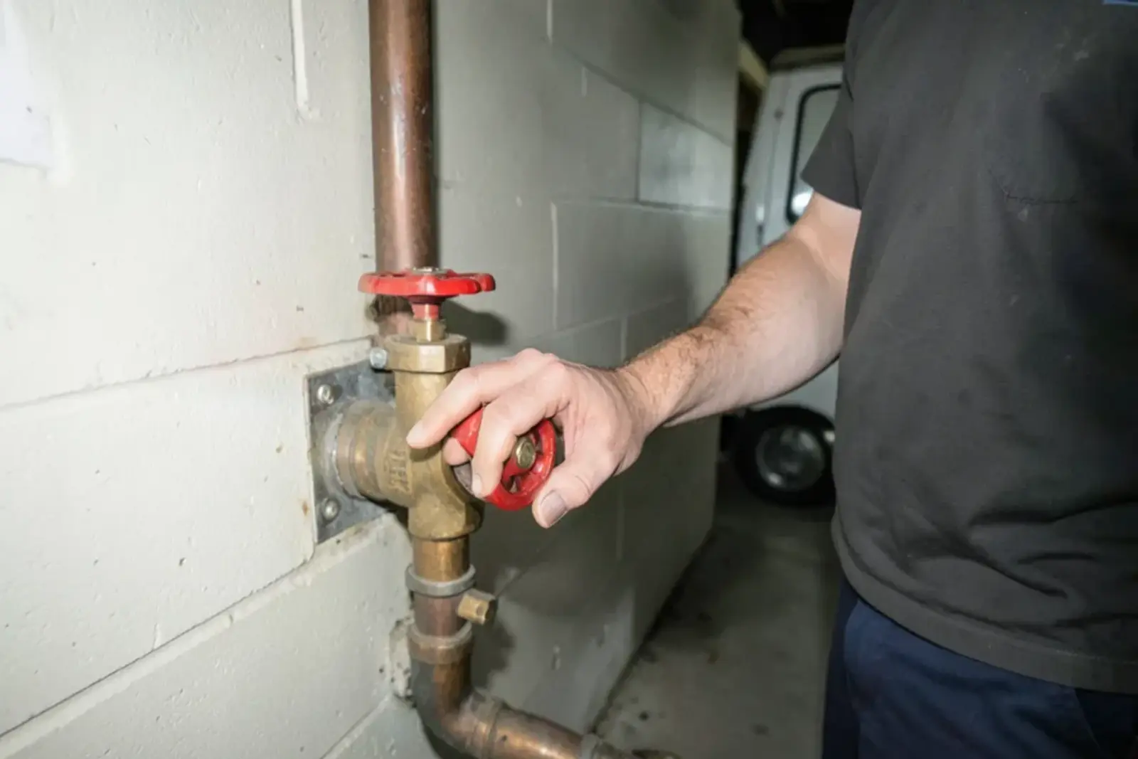 Hand turning a round red gate valve handle on the house side of a basement water meter